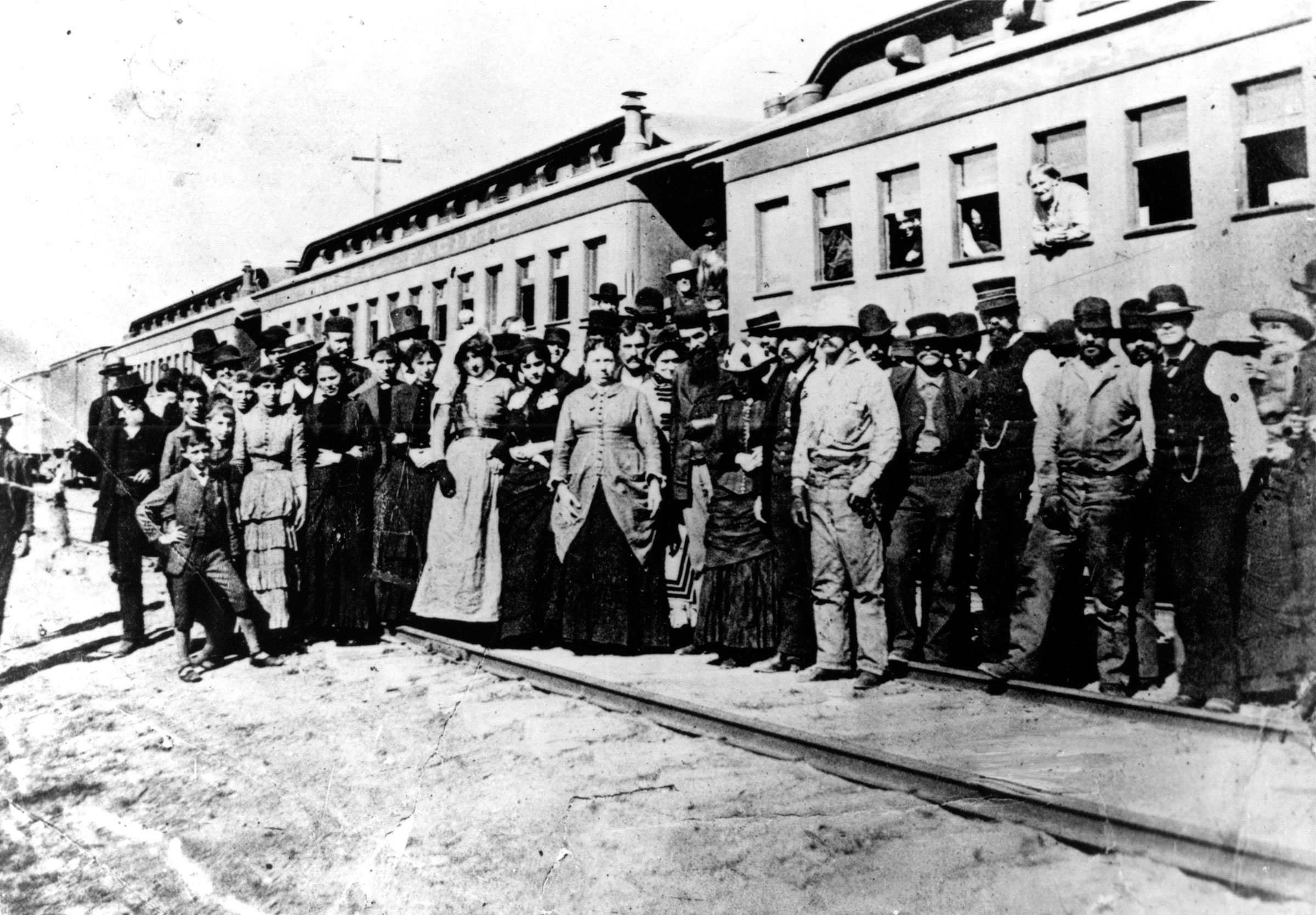 A group of immigrants pose beside a Central Pacific train stopped at Mill City, Nevada, en route to California in 1880.