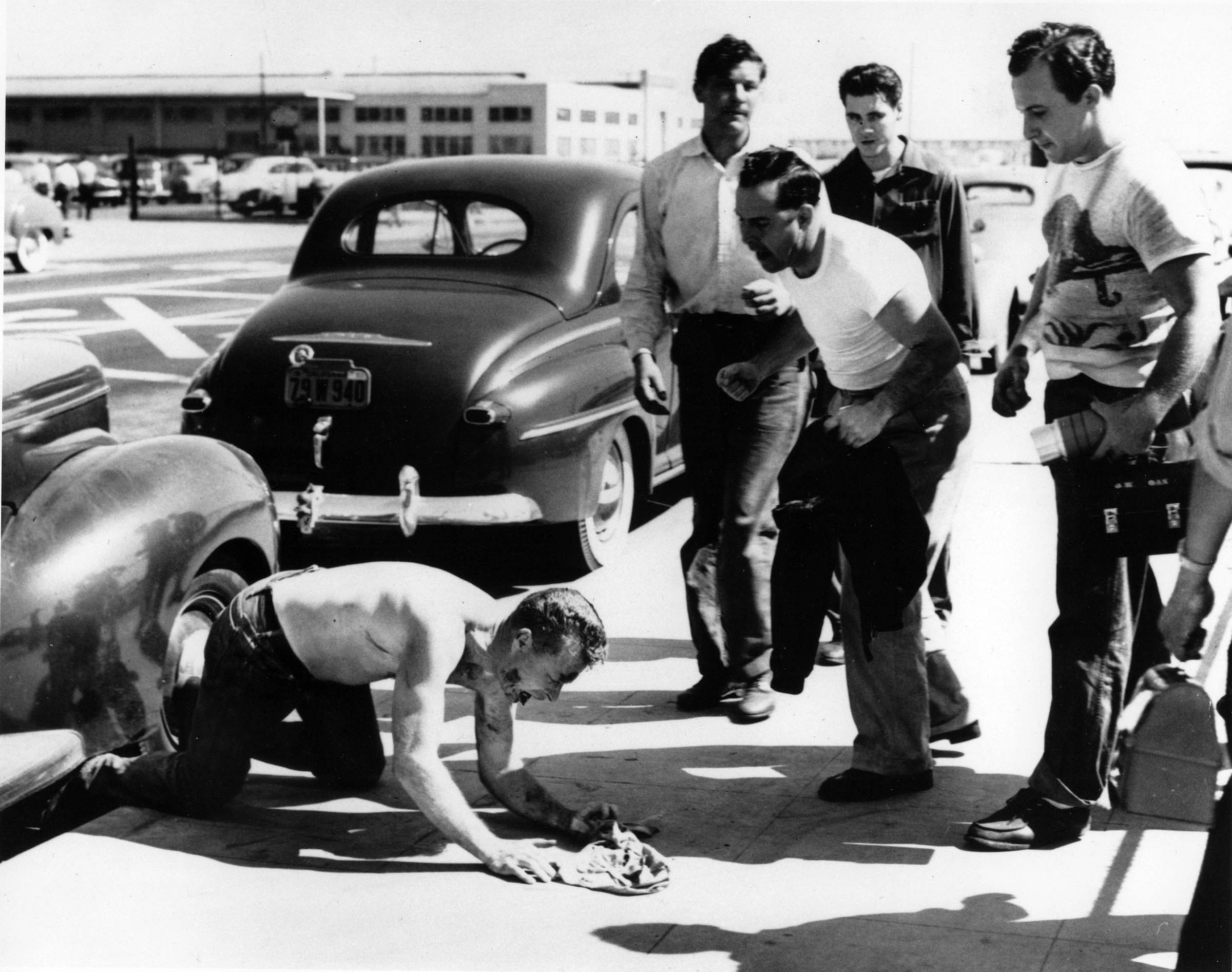 Autoworker Basil Gordon kneels on the sidewalk outside a Los Angeles Chrysler Corporation plant in July 1950 after receiving a beating from fellow workers. Gordon and two other workers were attacked when they refused to say whether they belonged to the Communist Party.