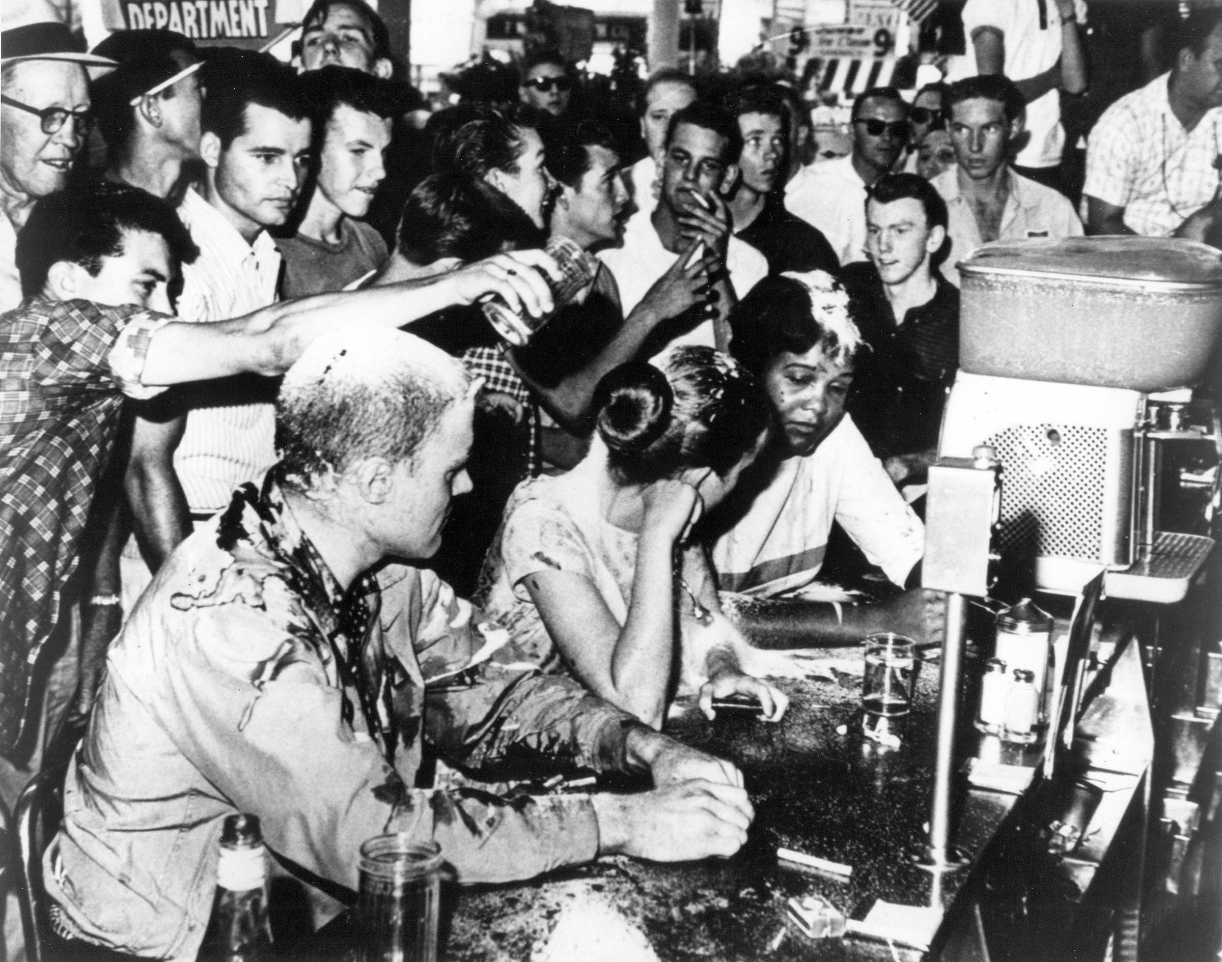 White youths shower abuse and food on a Tougaloo College professor and students who are staging a sit-in at a segregated lunch counter in Jackson, Mississippi. After soda, ketchup, mustard, and sugar failed to deter them, the civil rights demonstrators were doused with spray paint and beaten.