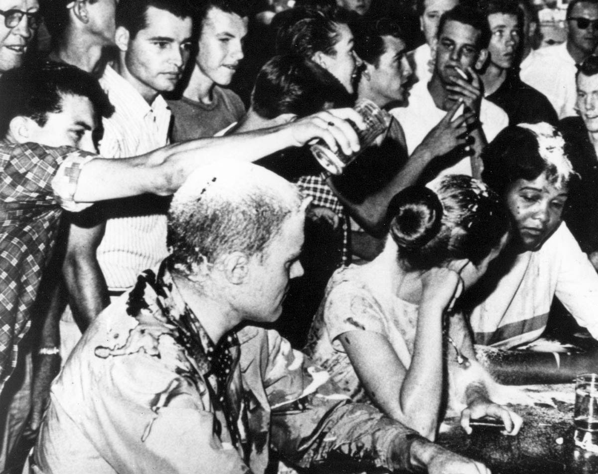 White youths shower abuse and food on a Tougaloo College professor and students who are staging a sit-in at a segregated lunch counter in Jackson, Mississippi. After soda, ketchup, mustard, and sugar failed to deter them, the civil rights demonstrators were doused with spray paint and beaten.