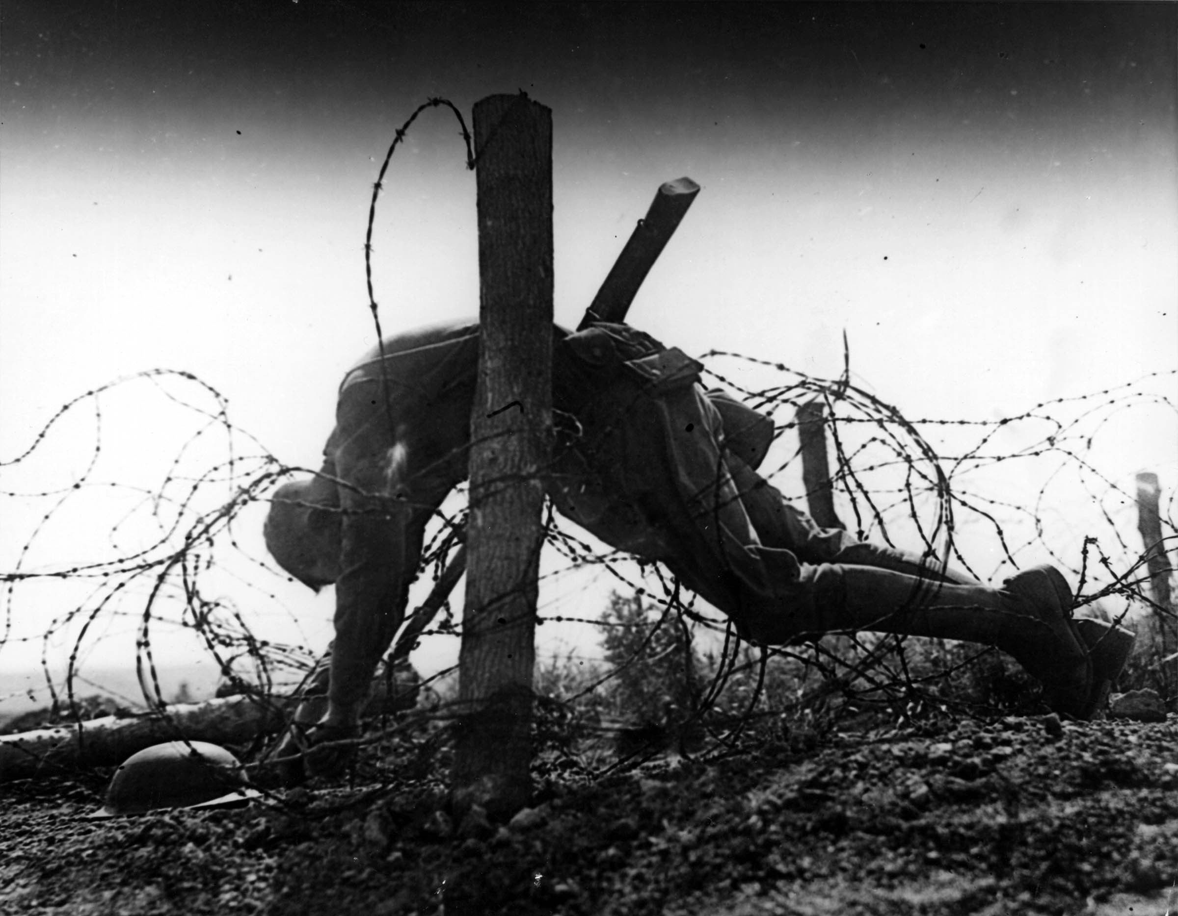 A soldier’s corpse, caught on one of the barbed-wire barricades that crisscrossed European battlefields during the First World War, hangs unburied between the trenches of the opposing armies.