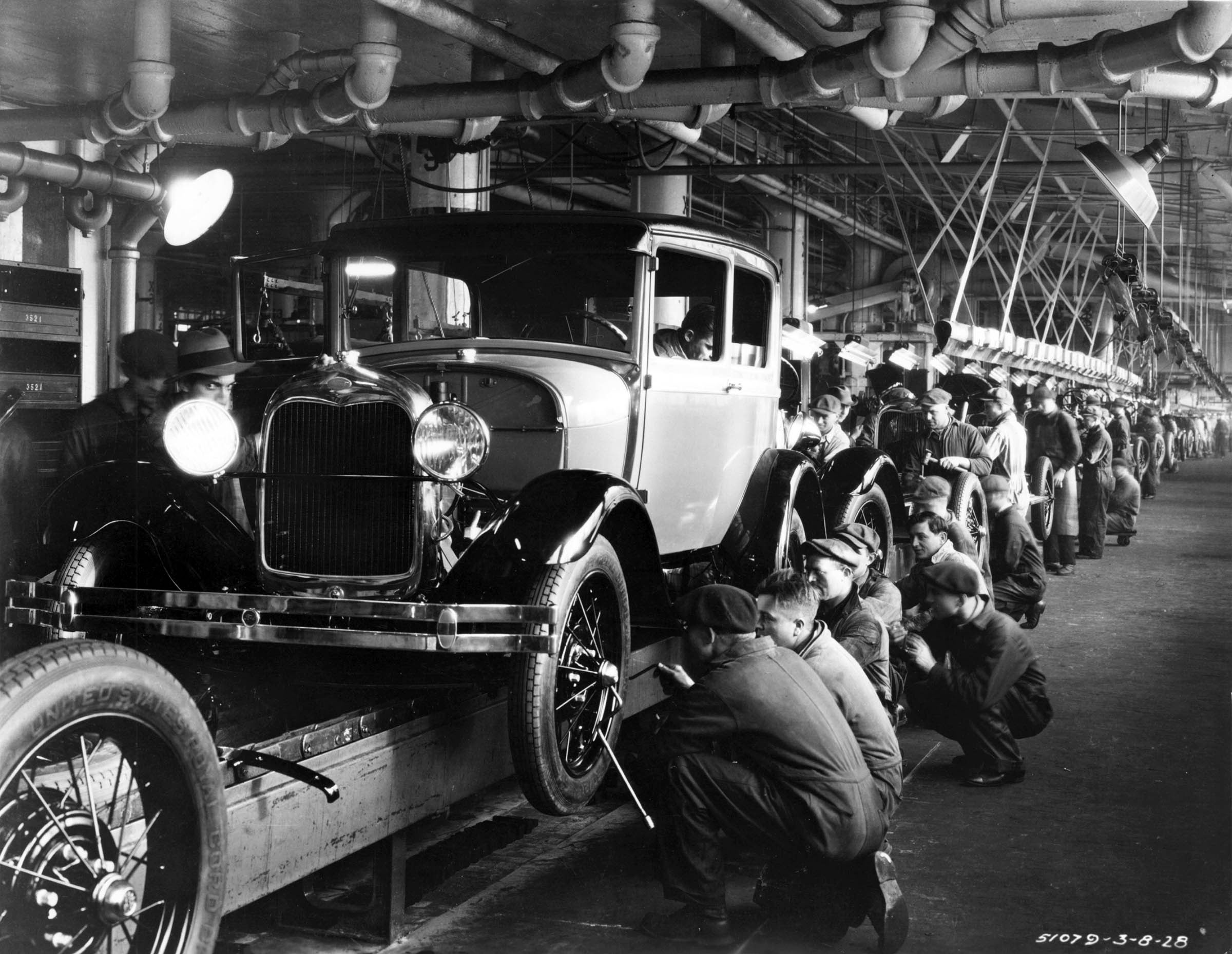 Automobile workers at the end of an assembly line at the Ford River Rouge plant are shown here putting the finishing touches on the stylish new Model A, which replaced the basic black Model T in 1927.