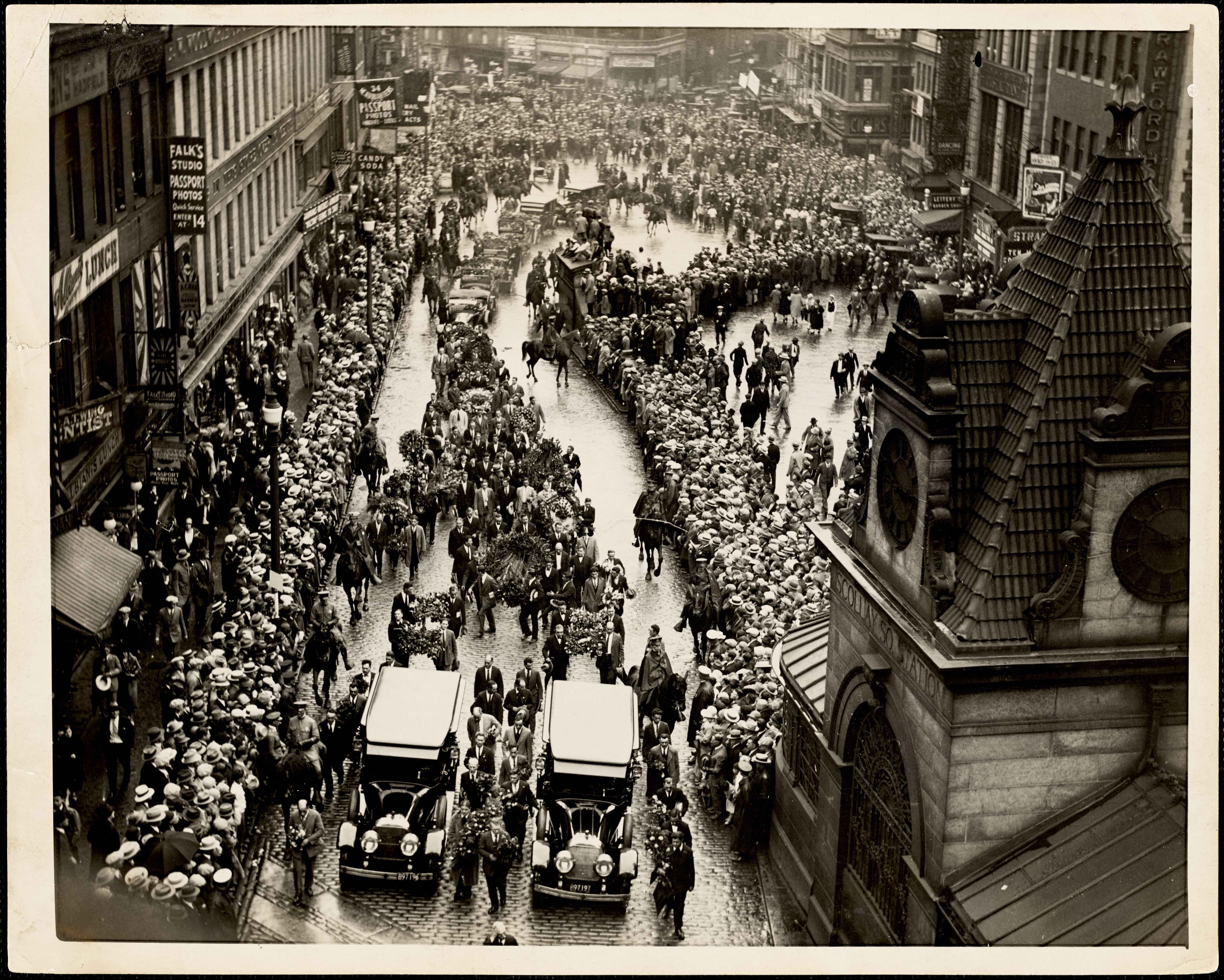 Thousands of mourners follow behind the funeral carriages of Sacco and Vanzetti.