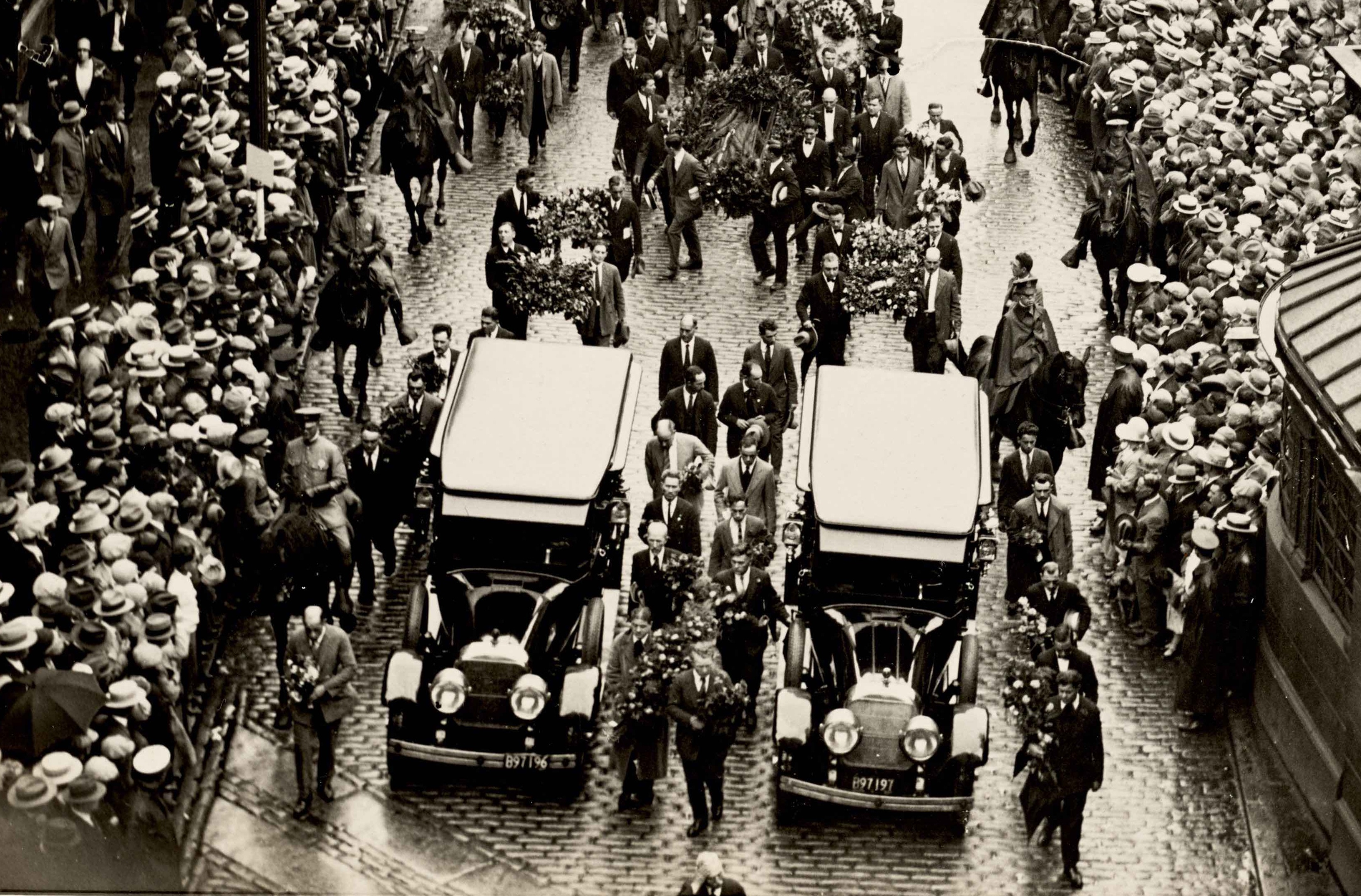 Thousands of mourners follow behind the funeral carriages of Sacco and Vanzetti.