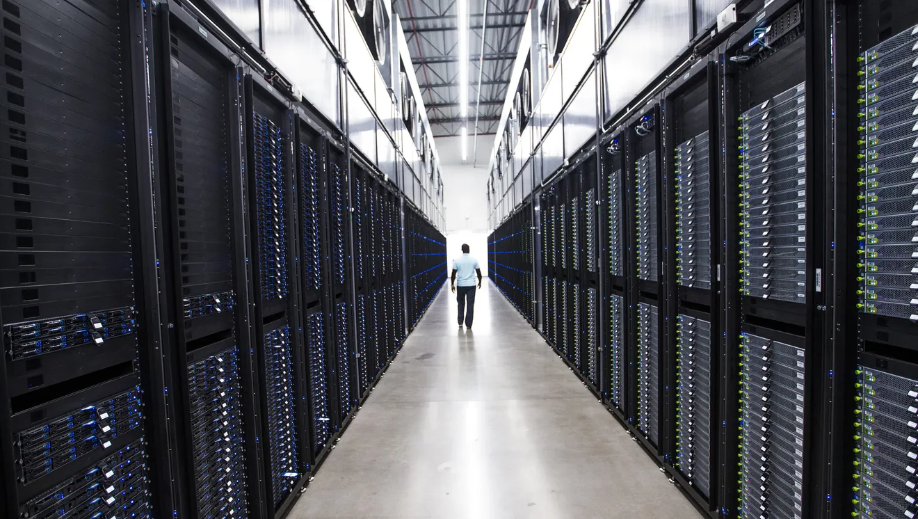 An Apple operations manager walks between looming servers in the company’s giant data center in Mesa, Arizona. Data centers—also known as server farms or server clusters—house thousands of computers that provide power for data-intensive and continually expanding online programs and services (such as Apple’s music and video streaming and cloud-storage services). As consumer and business demand increased, “hyper-scale” data centers have been constructed by Apple, Amazon, Google, Microsoft, and other major technology companies, doubling in number in the United States and abroad from three hundred in 2015 to twice as many only five years later. The proliferation of these farms came at a cost to both their locations and the climate in general. While typically offering few jobs, each center's multitude of servers generate so much heat they require cooling by three to five million gallons of water daily—comparable to a city of thirty thousand to fifty thousand people.